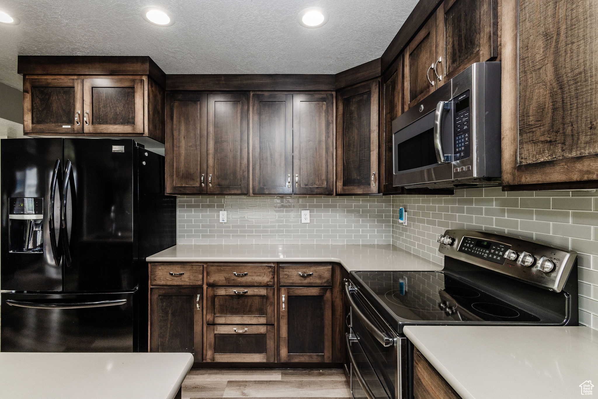 Kitchen featuring black refrigerator with ice dispenser, light hardwood / wood-style floors, range with electric cooktop, tasteful backsplash, and a textured ceiling