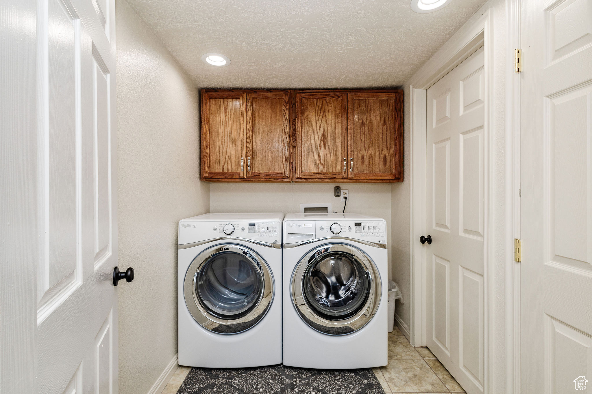 Laundry area featuring cabinets, light tile flooring, washer and clothes dryer, hookup for a washing machine, and a textured ceiling