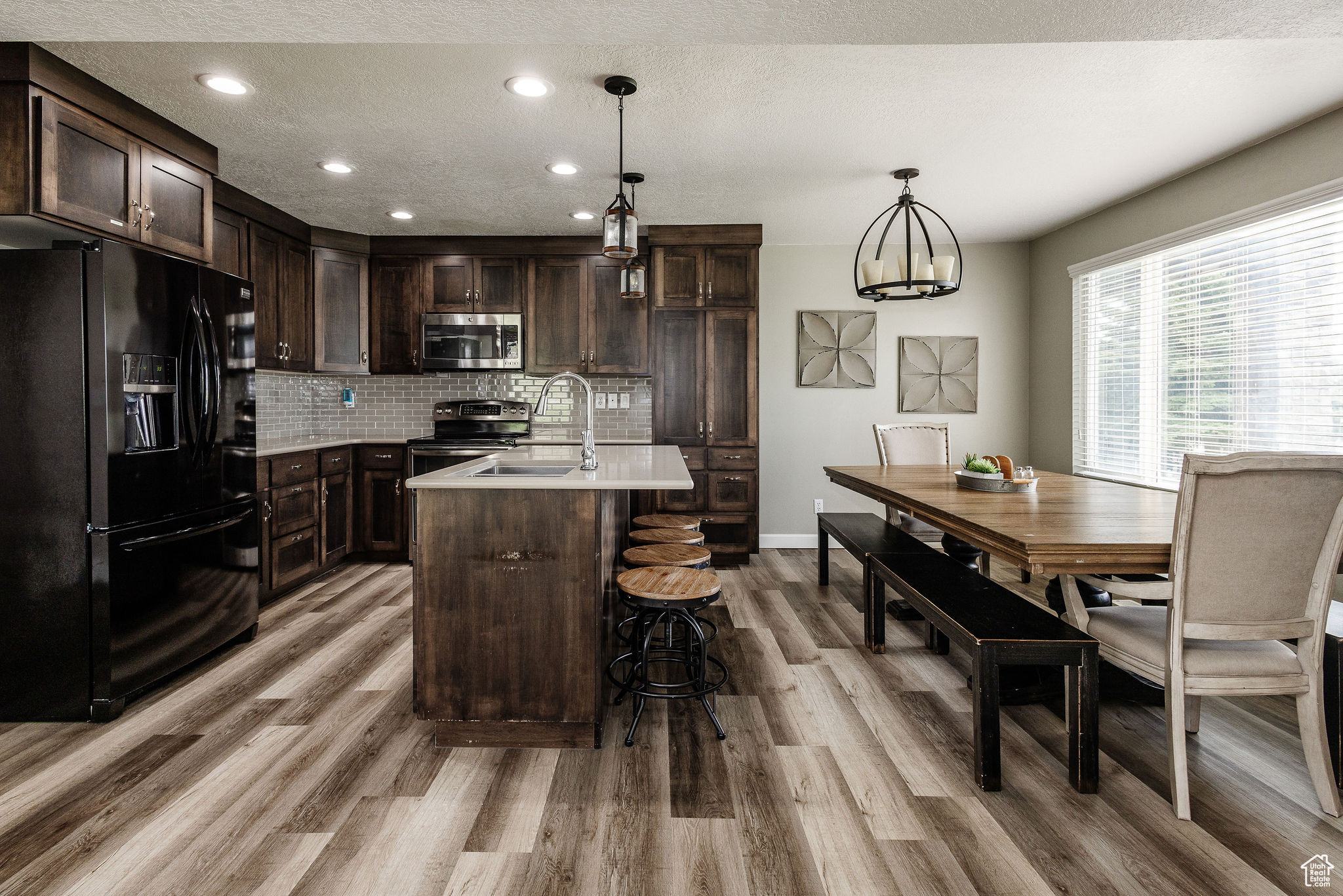 Kitchen featuring tasteful backsplash, an island with sink, light wood-type flooring, appliances with stainless steel finishes, and pendant lighting