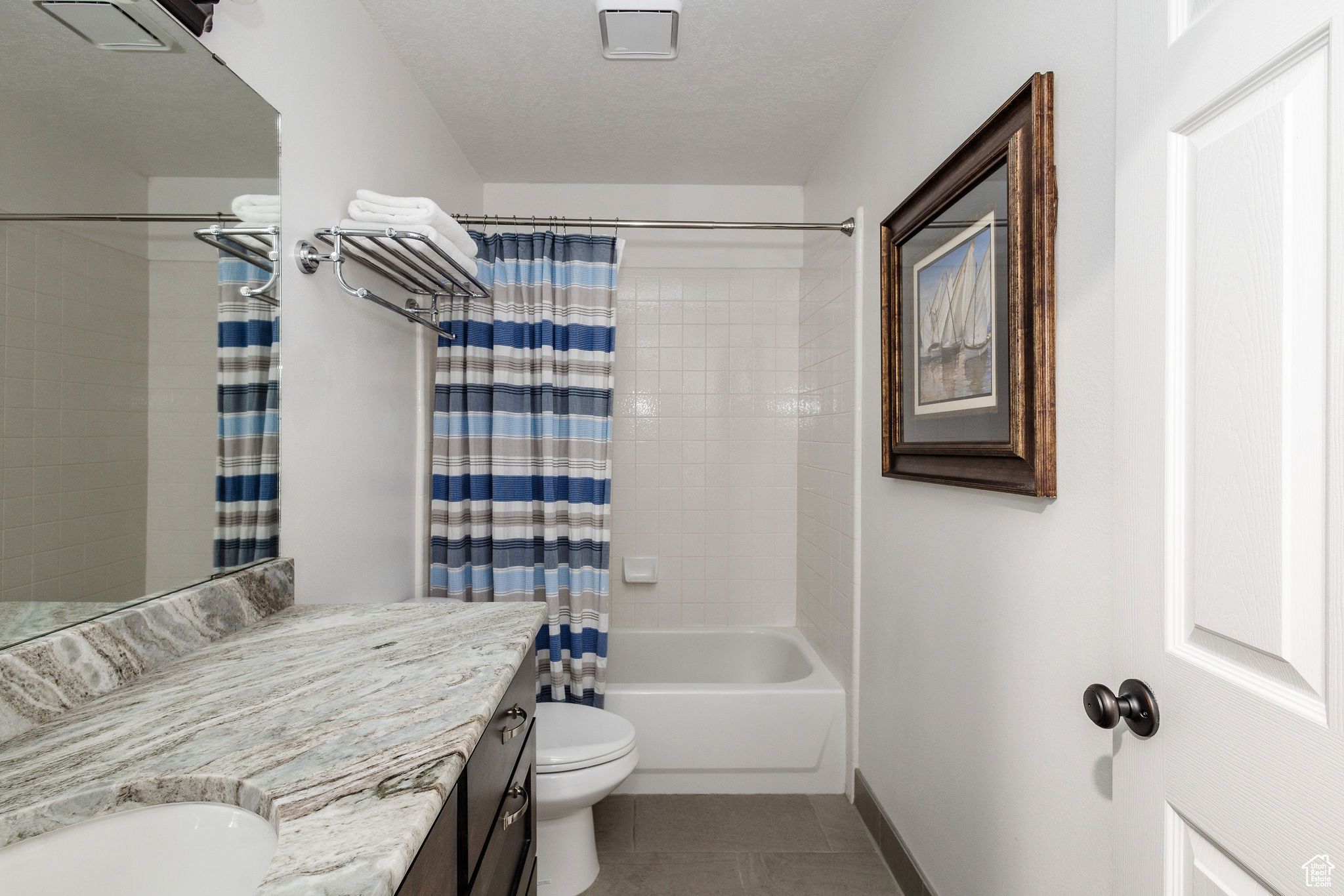 Full bathroom featuring a textured ceiling, shower / bath combo with shower curtain, tile floors, vanity, and toilet