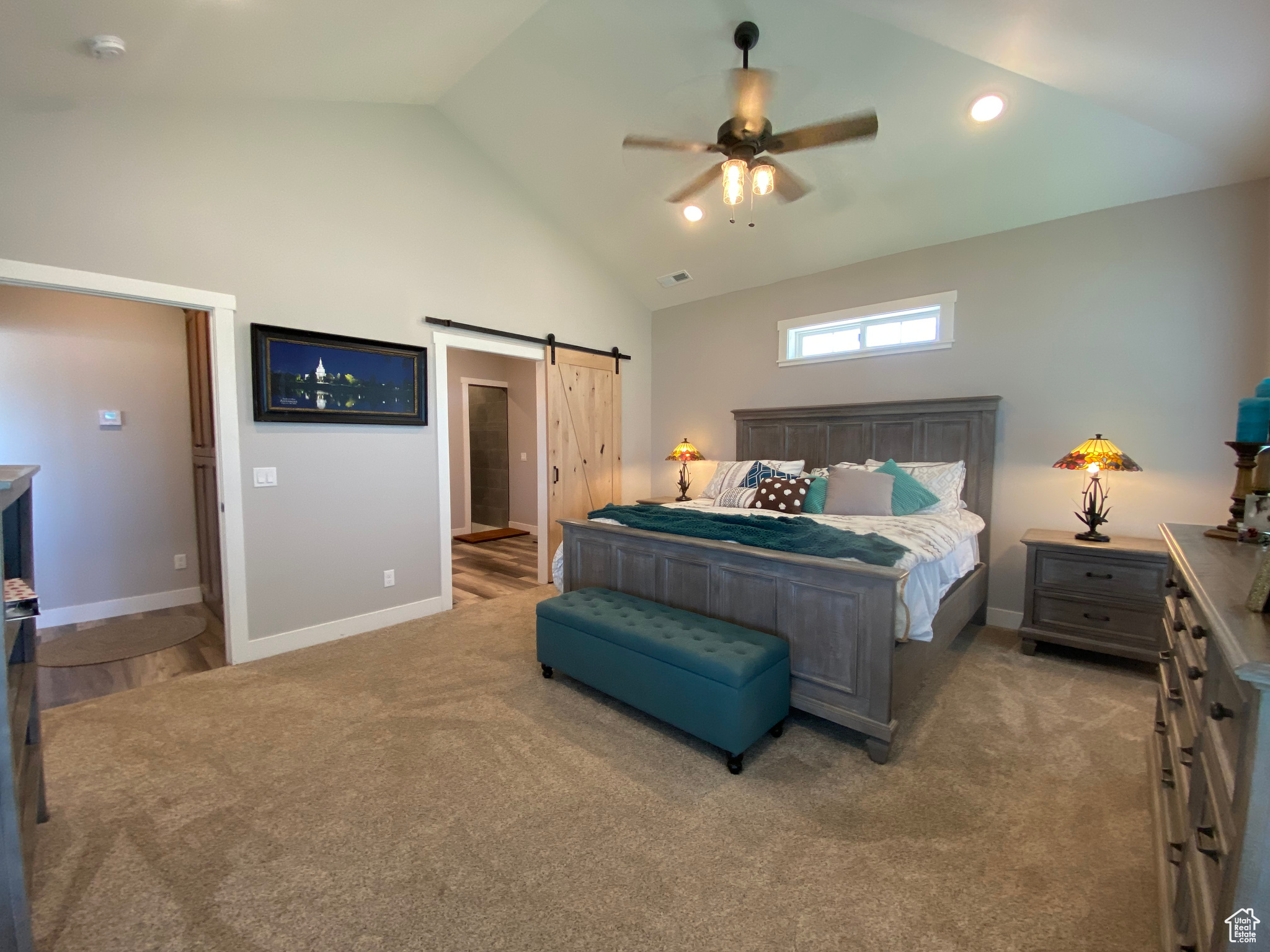 Bedroom featuring a barn door, dark colored carpet, ceiling fan, and high vaulted ceiling