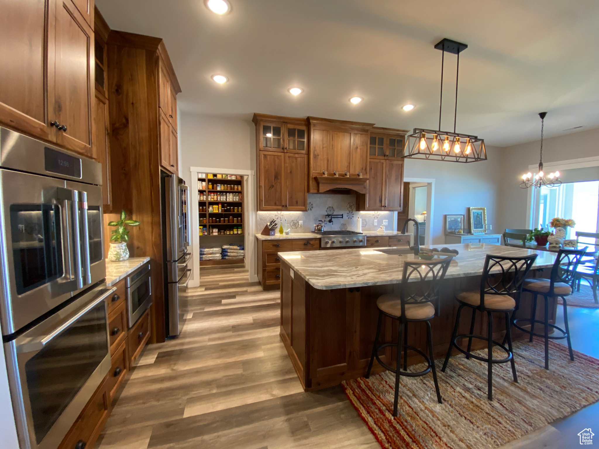 Kitchen featuring decorative light fixtures, light stone counters, stainless steel appliances, an island with sink, and wood-type flooring