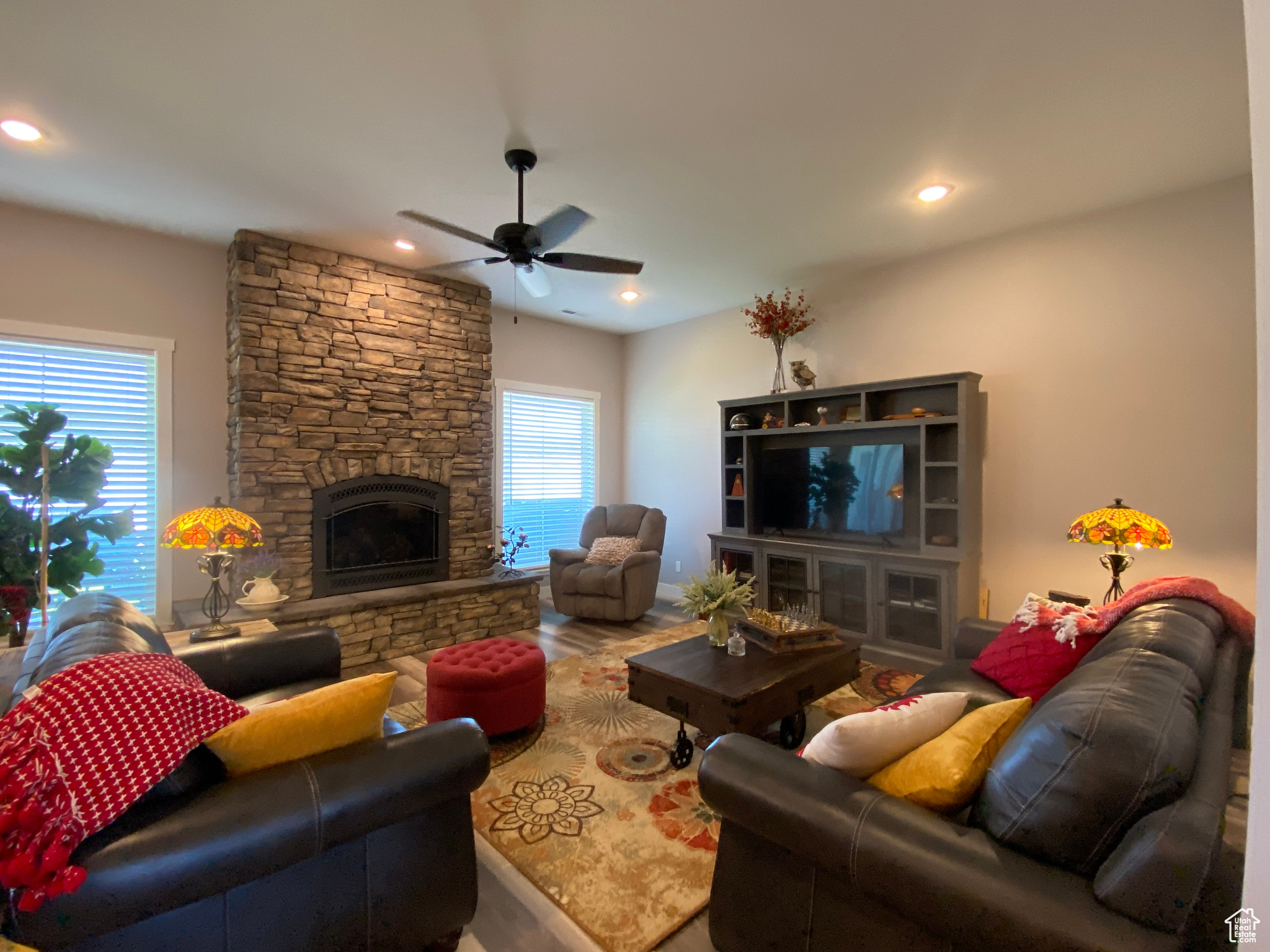 Living room with a stone fireplace, ceiling fan, hardwood / wood-style flooring, and a wealth of natural light