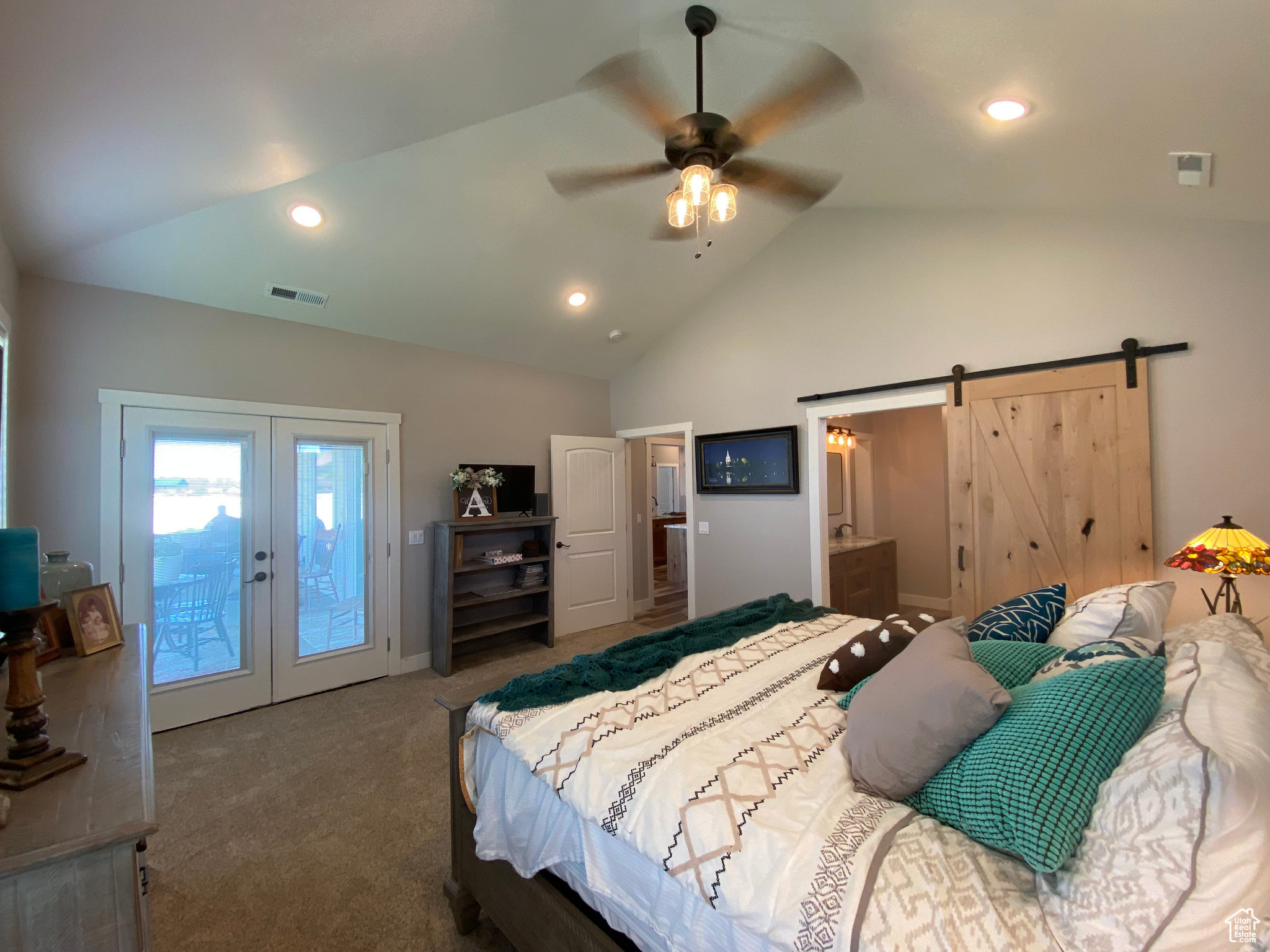 Carpeted bedroom with vaulted ceiling, access to exterior, ceiling fan, a barn door, and french doors