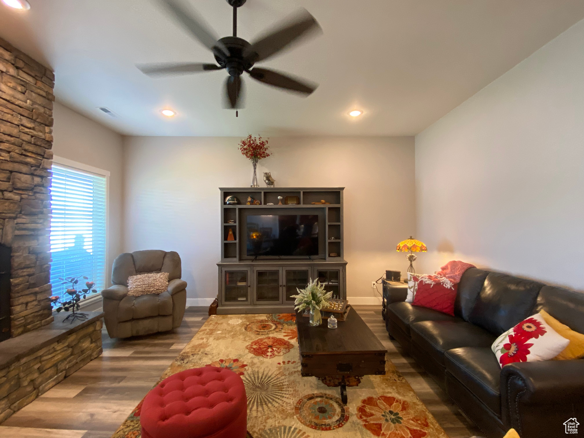 Living room with ceiling fan, a stone fireplace, and hardwood / wood-style flooring