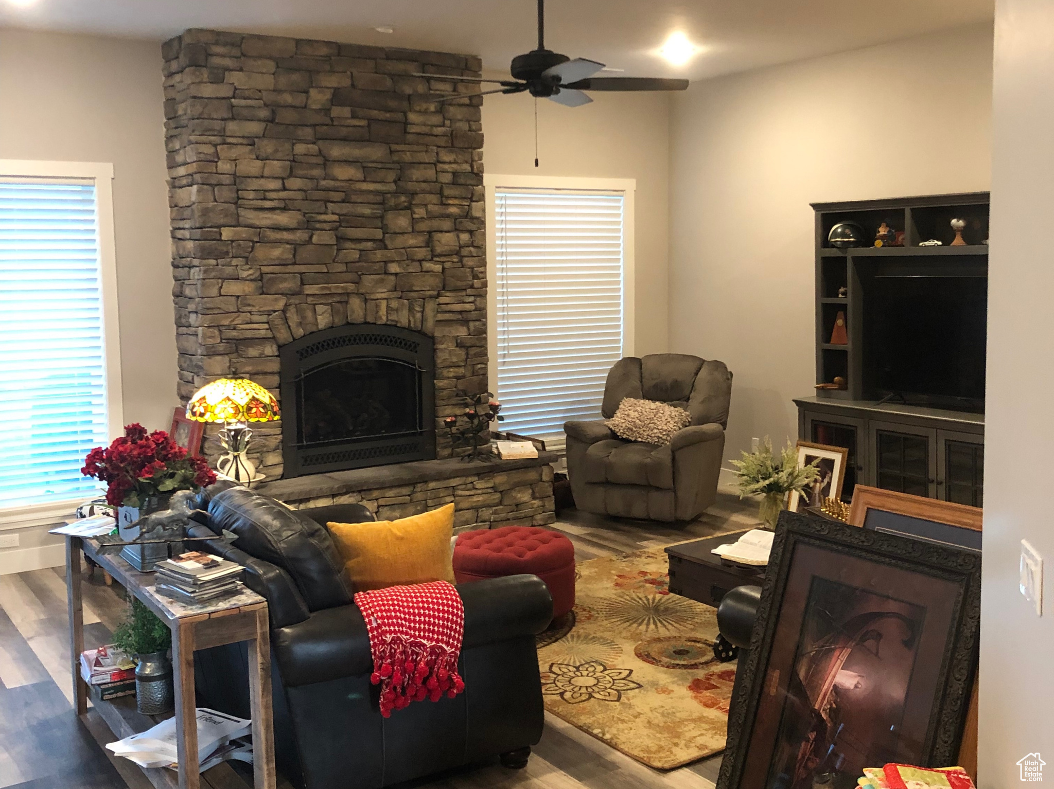 Living room featuring a stone fireplace, wood-type flooring, and ceiling fan