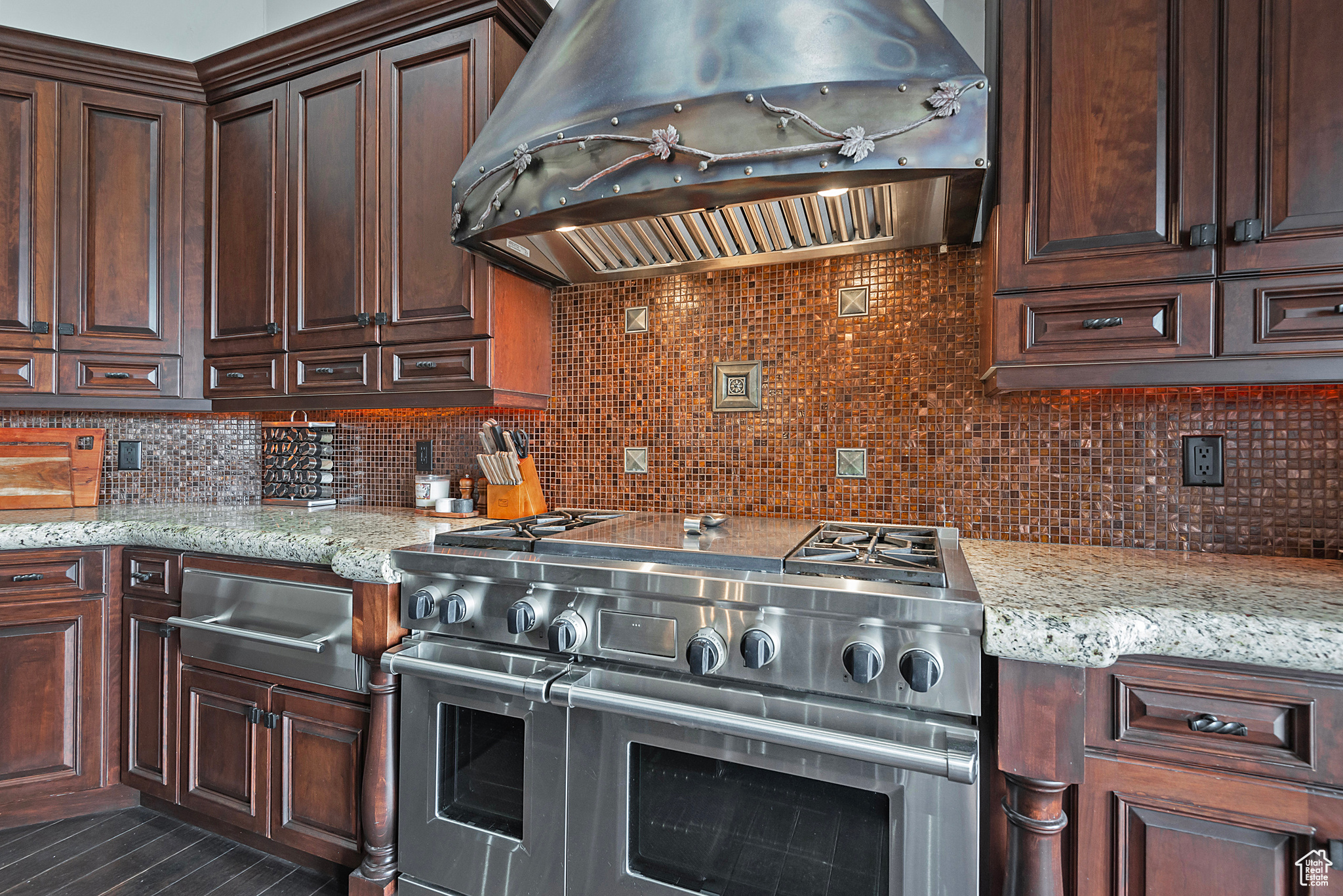 Kitchen with wall chimney range hood, backsplash, range with two ovens, and light stone counters