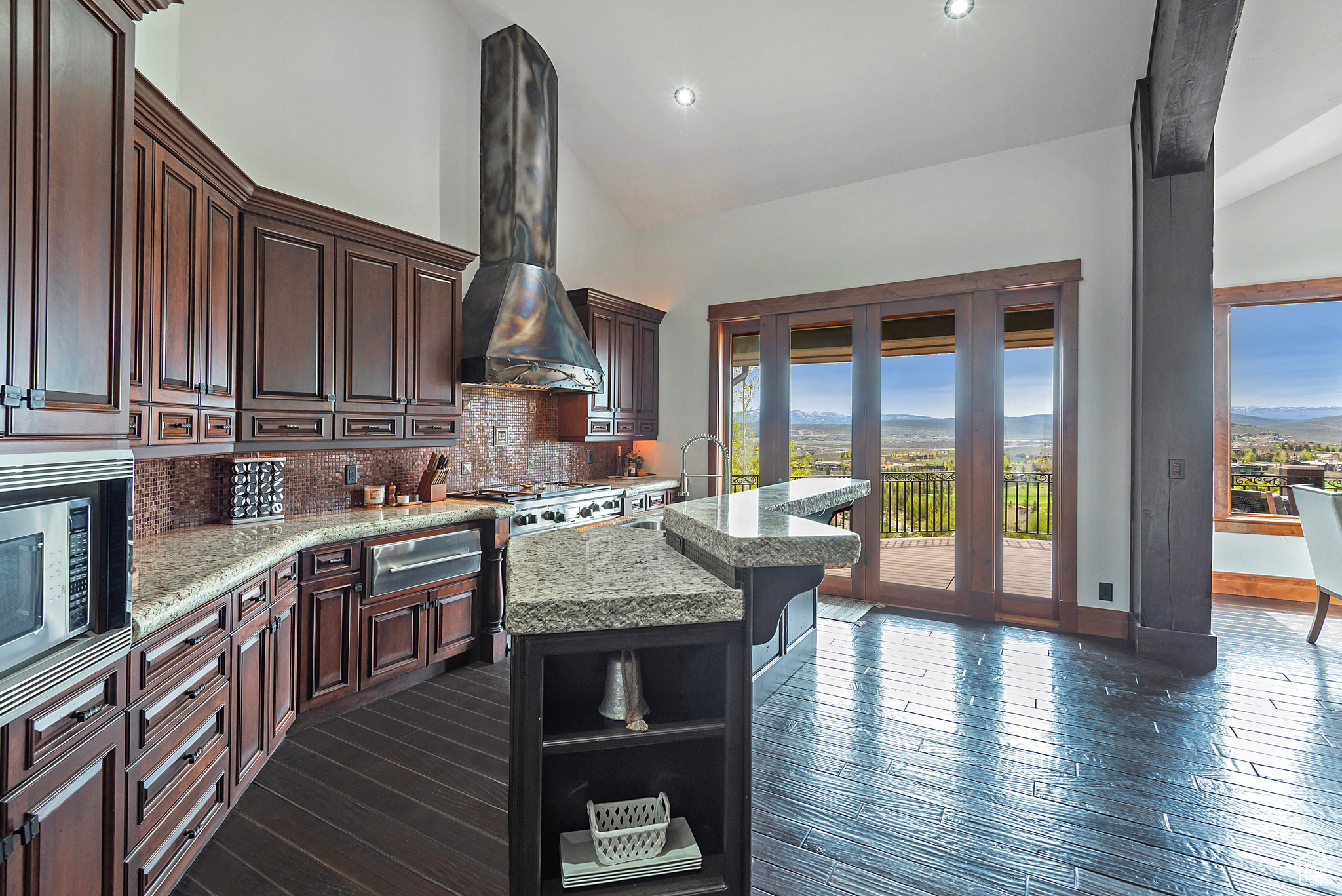 Kitchen with a center island with sink, dark hardwood / wood-style flooring, light stone counters, wall chimney exhaust hood, and tasteful backsplash