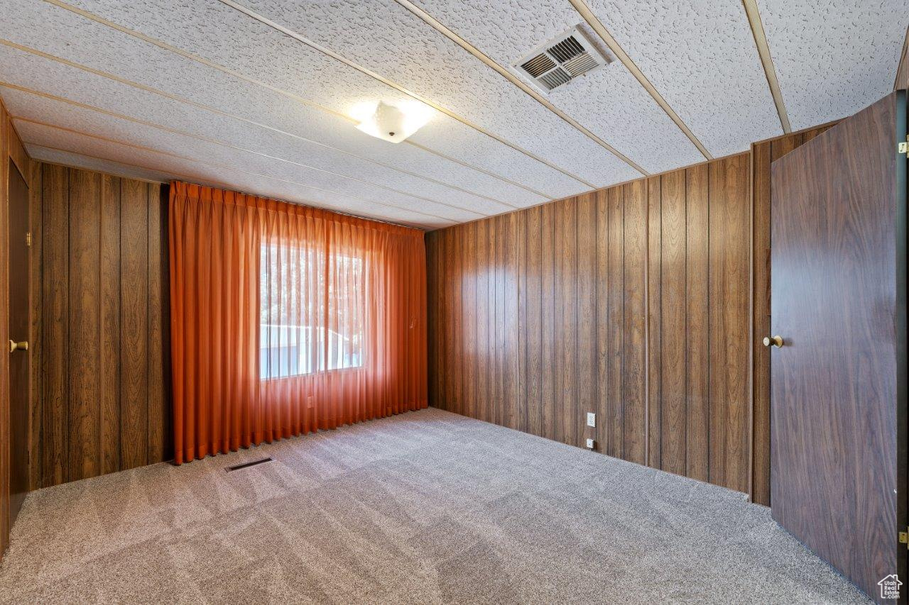 Unfurnished room with a textured ceiling, carpet flooring, and wood walls