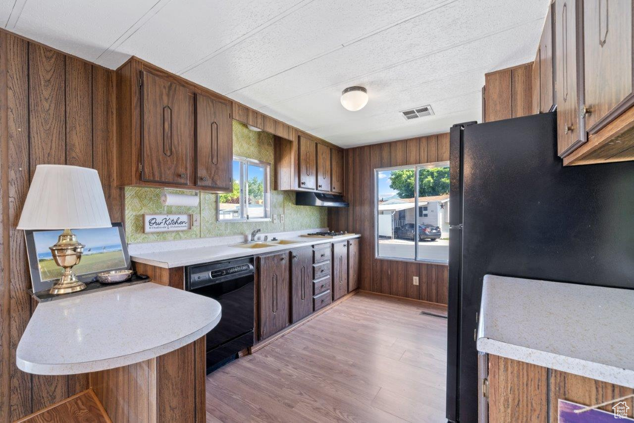 Kitchen featuring backsplash, black appliances, light wood-type flooring, sink, and wooden walls