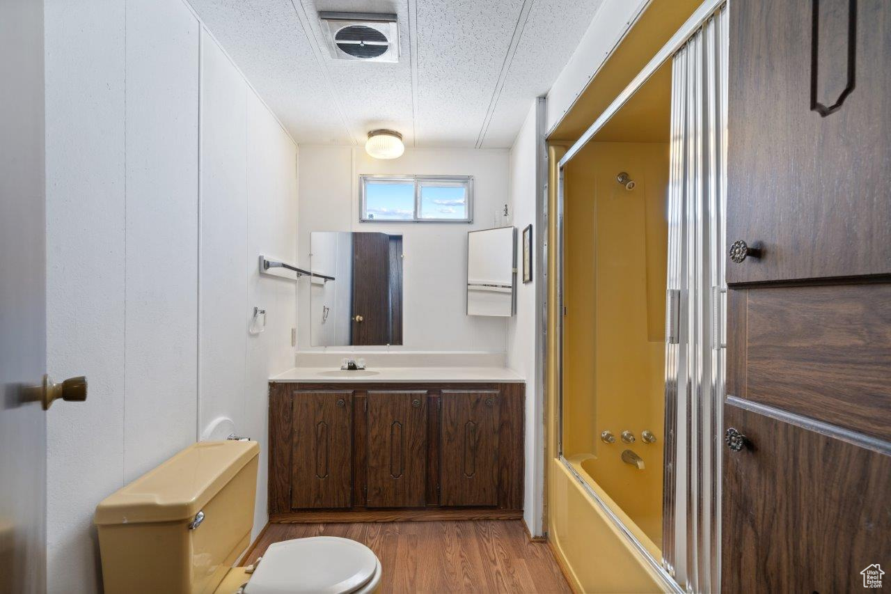 Full bathroom featuring shower / bath combination with glass door, toilet, hardwood / wood-style floors, vanity, and a textured ceiling