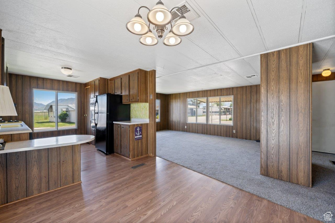 Kitchen with a notable chandelier, black refrigerator, hardwood / wood-style floors, and wood walls