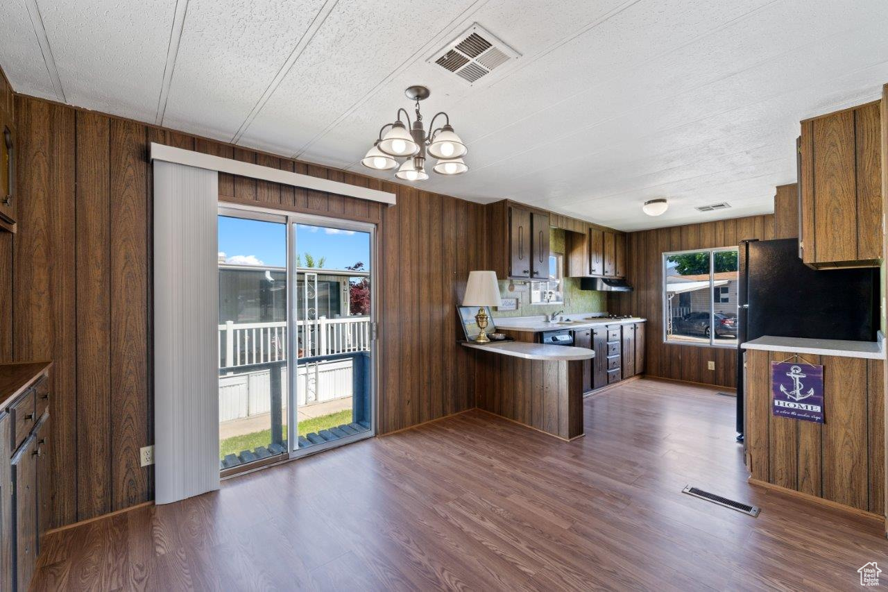 Kitchen featuring a textured ceiling, dark hardwood / wood-style floors, decorative light fixtures, wood walls, and a chandelier