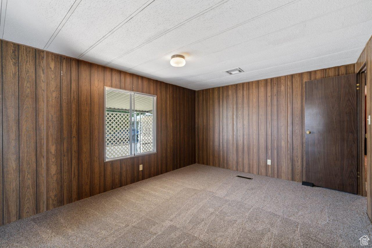 Empty room with wooden walls, a textured ceiling, and carpet floors