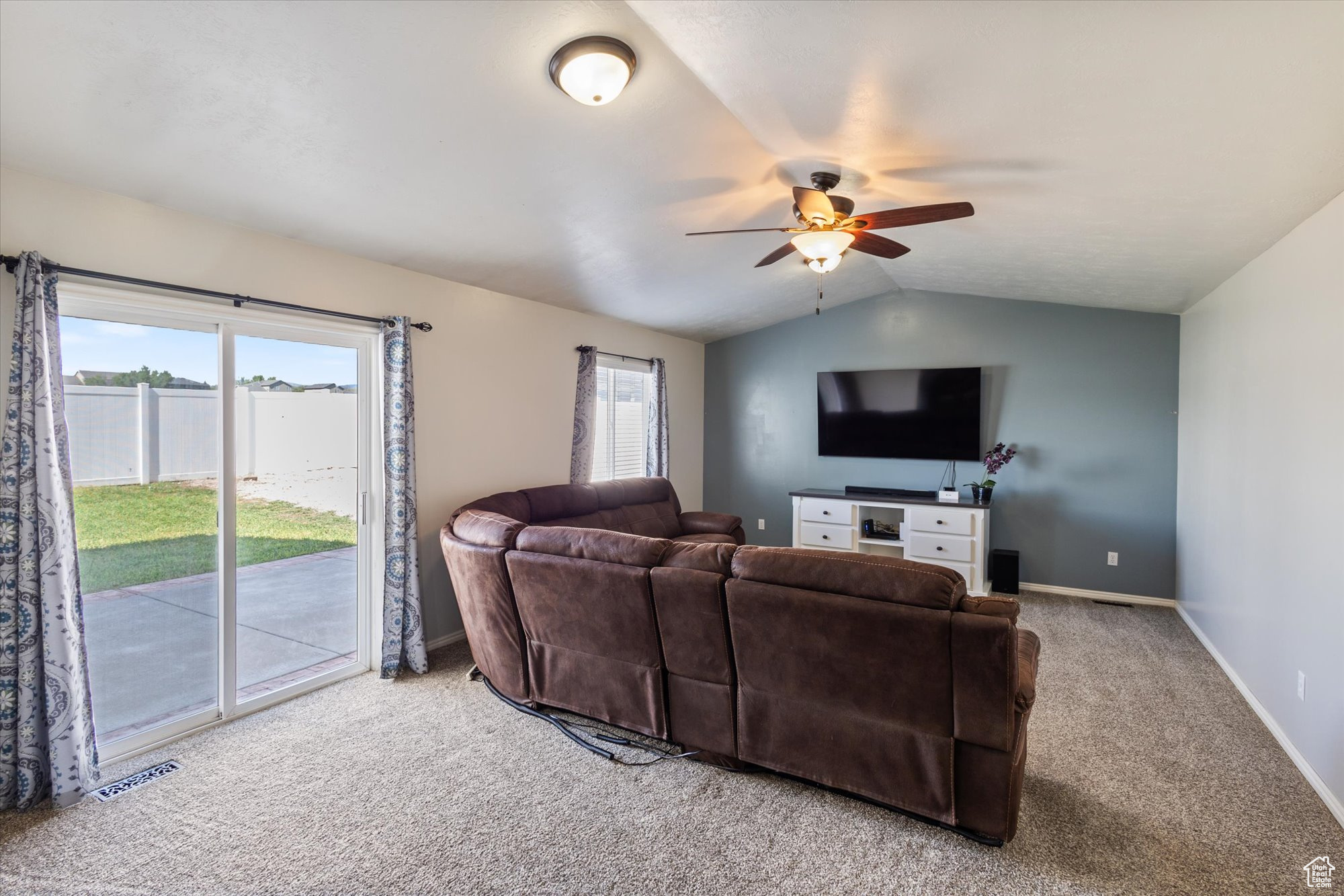 Carpeted living room with ceiling fan and lofted ceiling