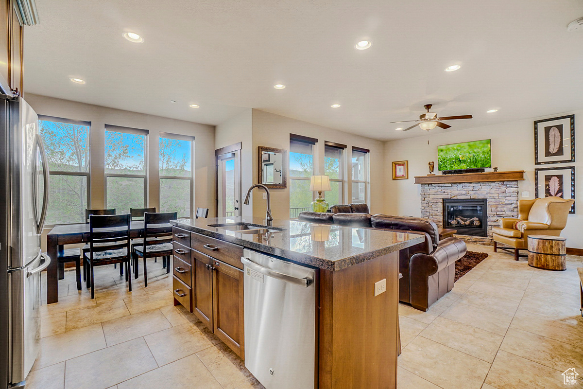 Kitchen featuring a fireplace, stainless steel appliances, a kitchen island with sink, ceiling fan, and light tile floors