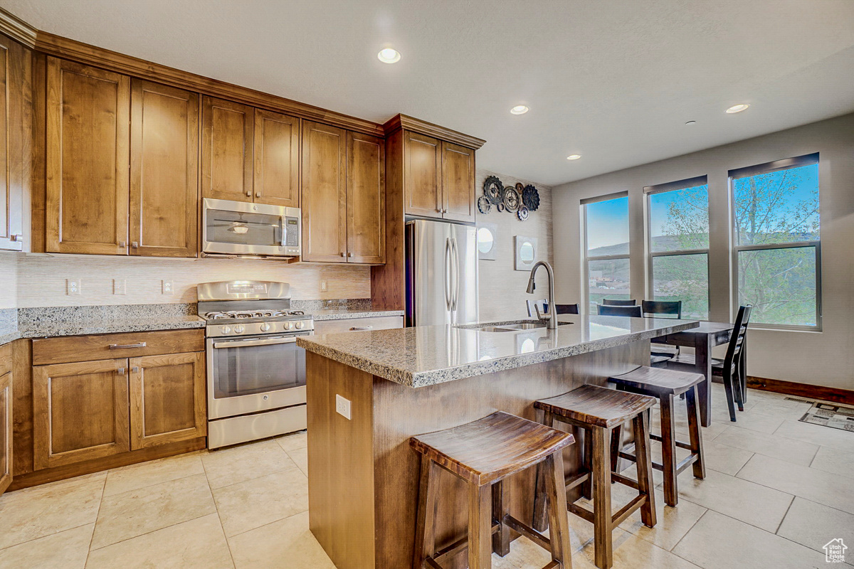 Kitchen featuring stainless steel appliances, sink, light tile flooring, and a kitchen island with sink