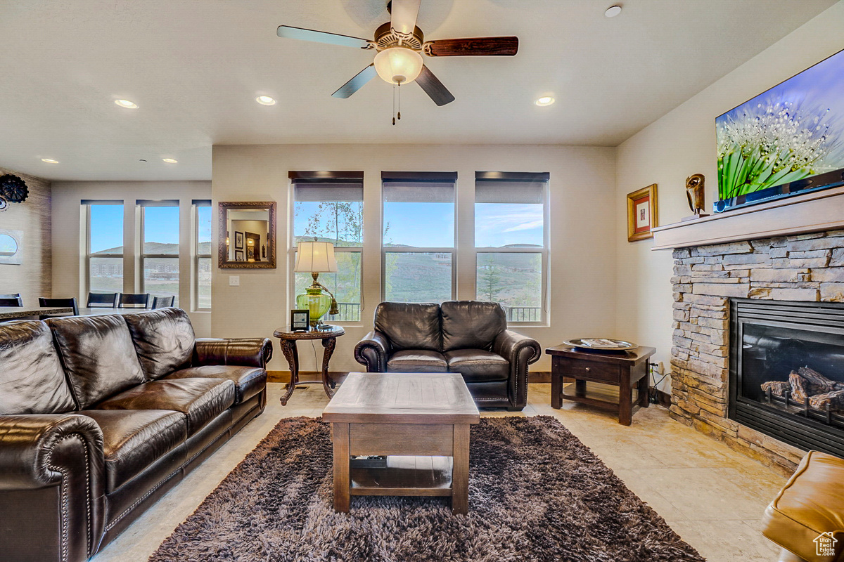 Living room with a stone fireplace, ceiling fan, and light tile flooring