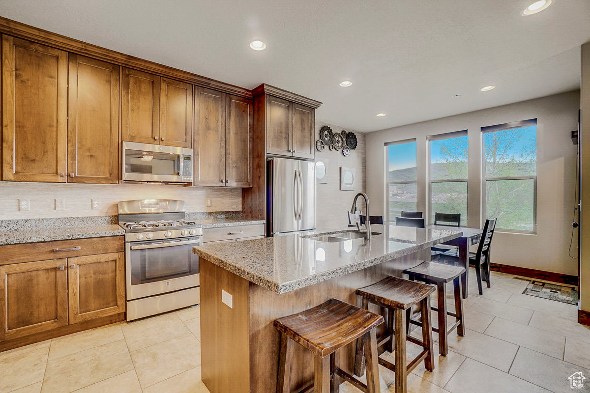 Kitchen featuring light stone countertops, stainless steel appliances, a kitchen island with sink, and light tile floors