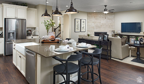 Kitchen featuring a fireplace, dark wood-type flooring, appliances with stainless steel finishes, a kitchen island with sink, and ceiling fan