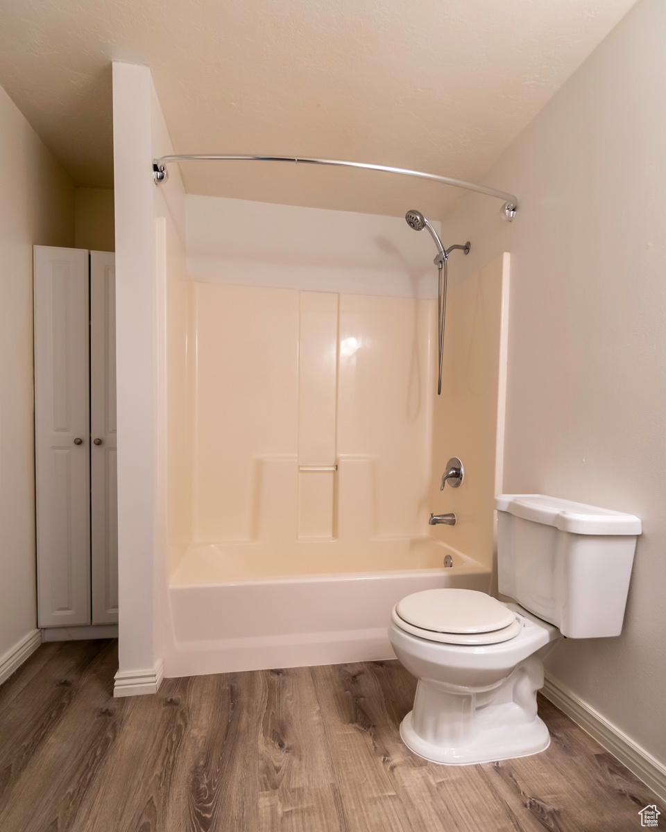 Bathroom with washtub / shower combination, hardwood / wood-style flooring, and toilet