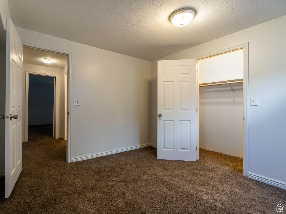 Unfurnished bedroom with a textured ceiling, a closet, and dark colored carpet