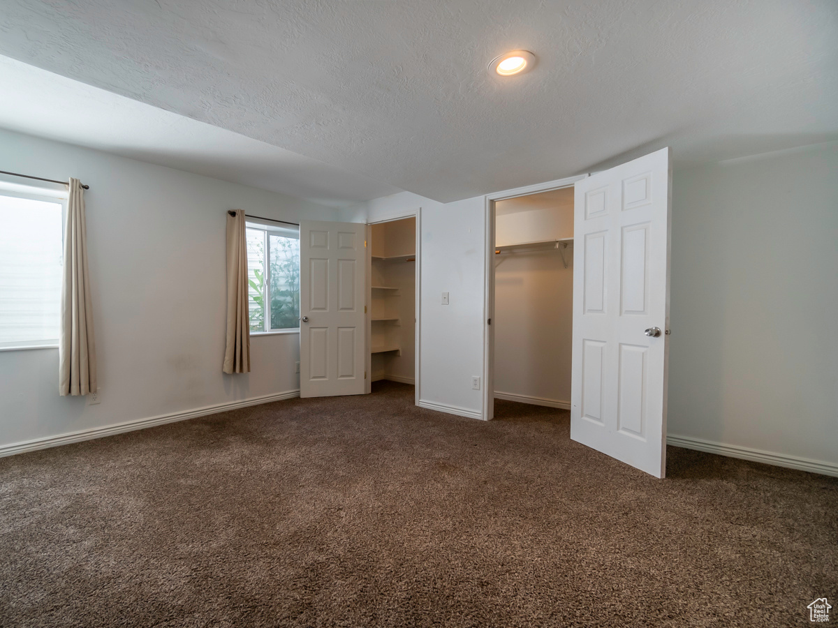 Unfurnished bedroom featuring a textured ceiling, a walk in closet, and dark carpet