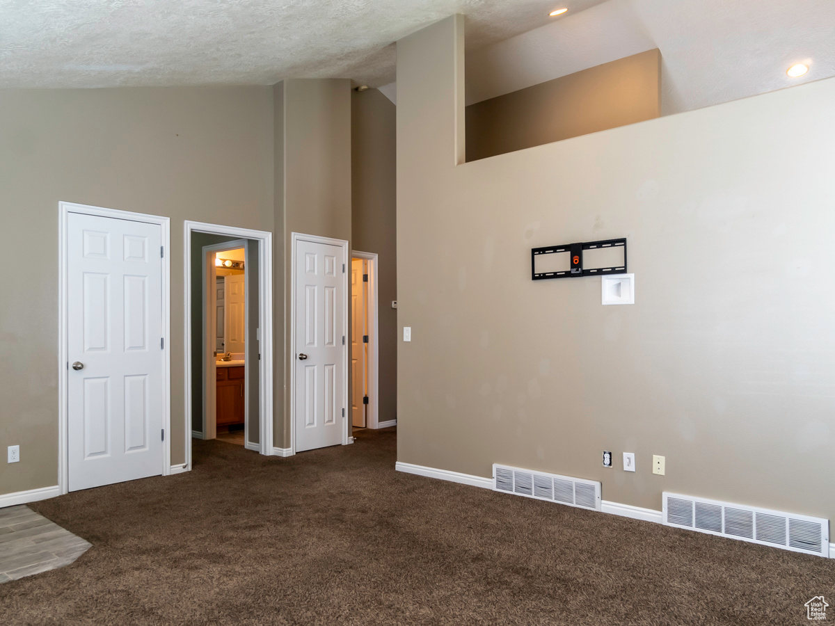 Interior space featuring high vaulted ceiling, dark colored carpet, and a textured ceiling