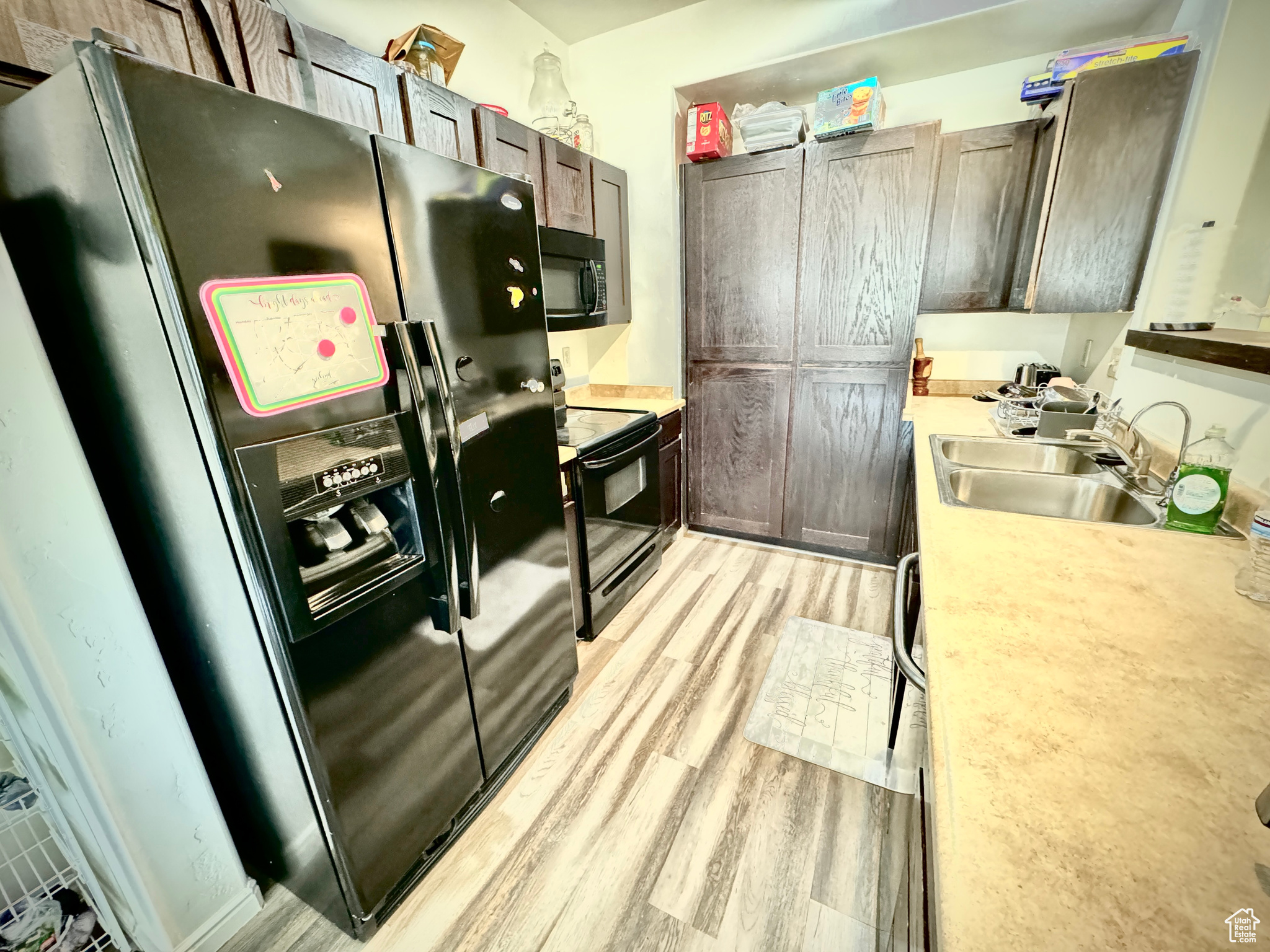 Kitchen featuring black appliances, sink, light hardwood / wood-style floors, and dark brown cabinets