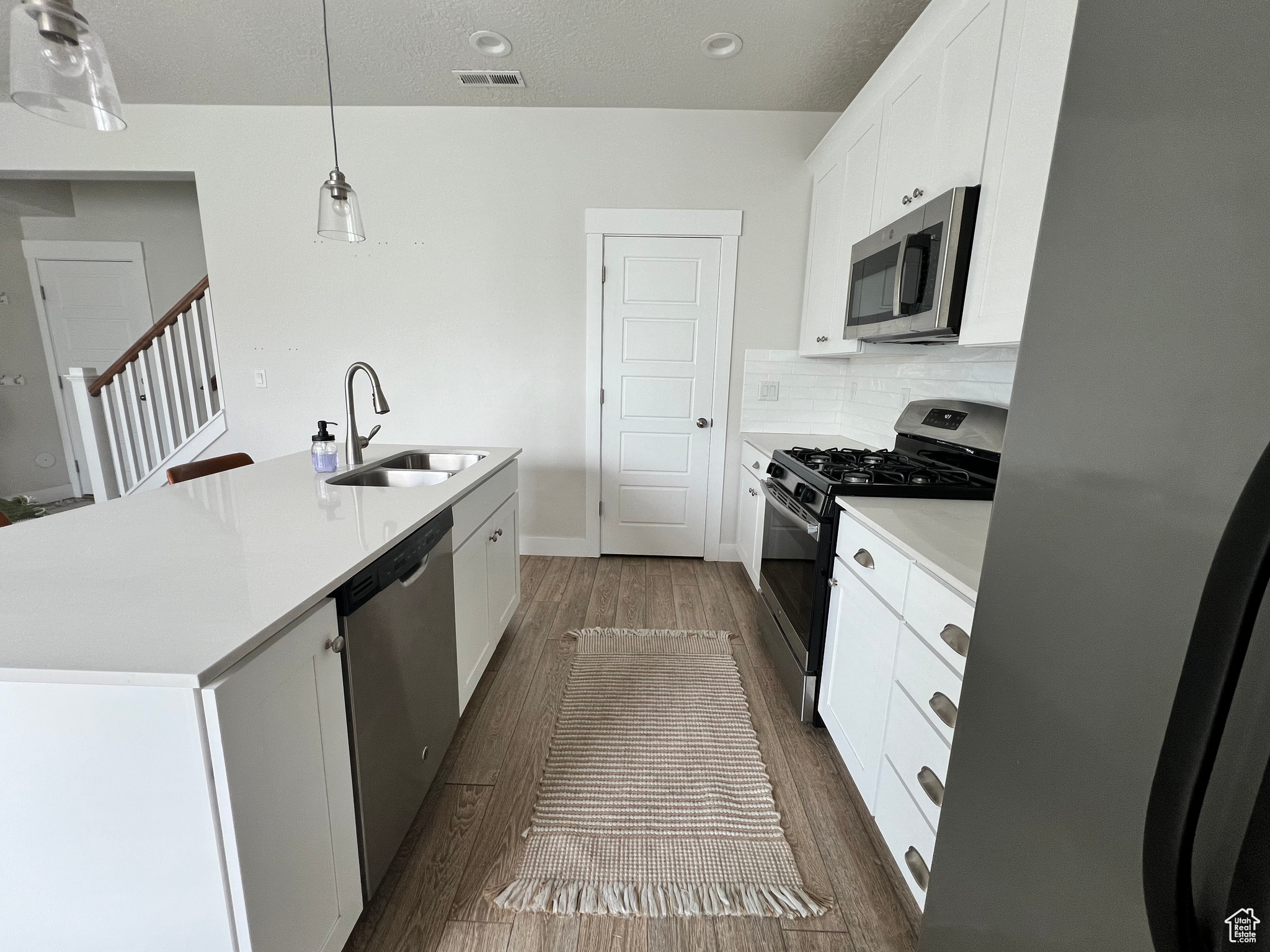 Kitchen featuring appliances with stainless steel finishes, dark wood-type flooring, tasteful backsplash, and a center island with sink