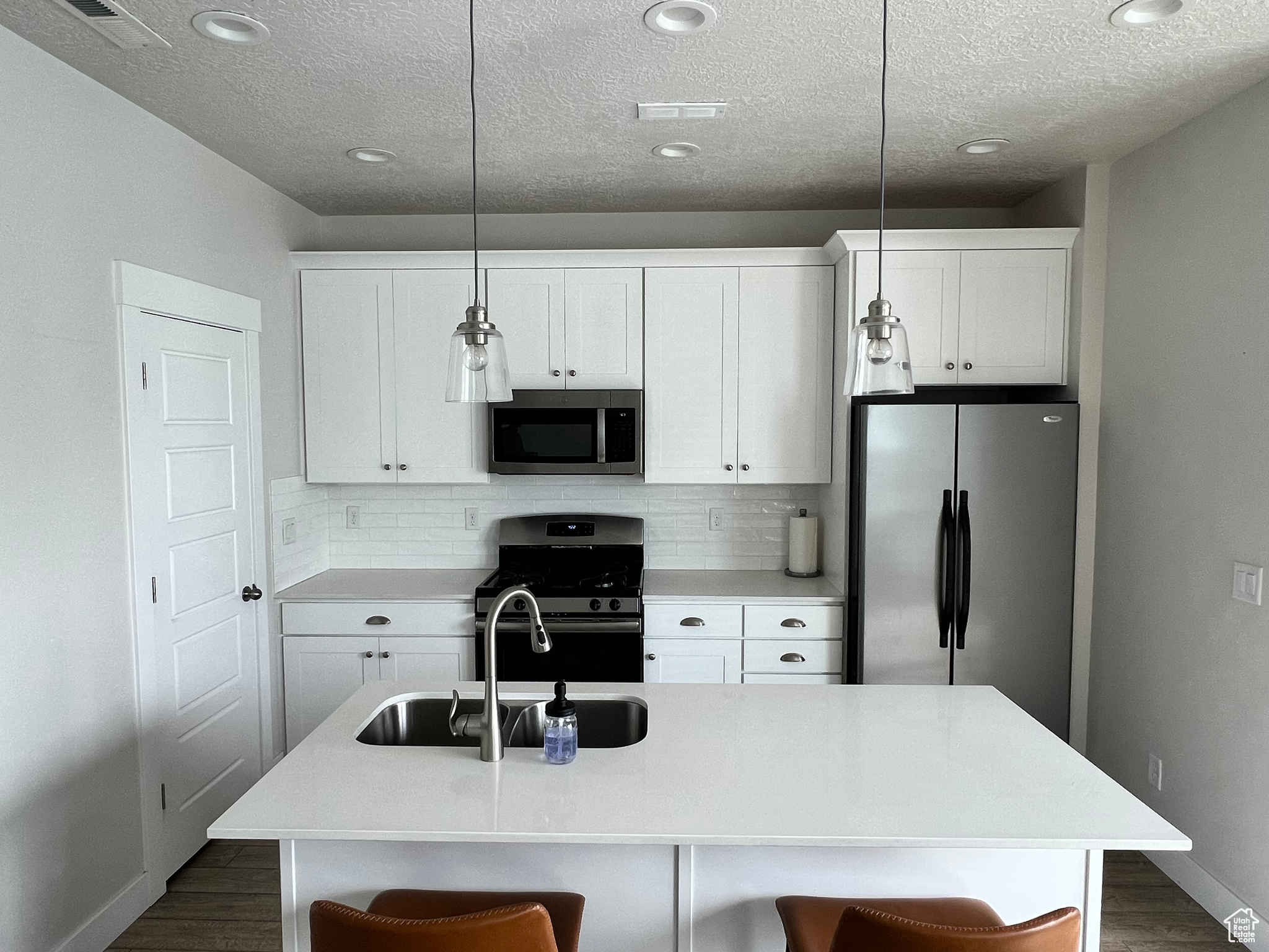 Kitchen with hanging light fixtures, a center island with sink, stainless steel appliances, dark hardwood / wood-style floors, and backsplash