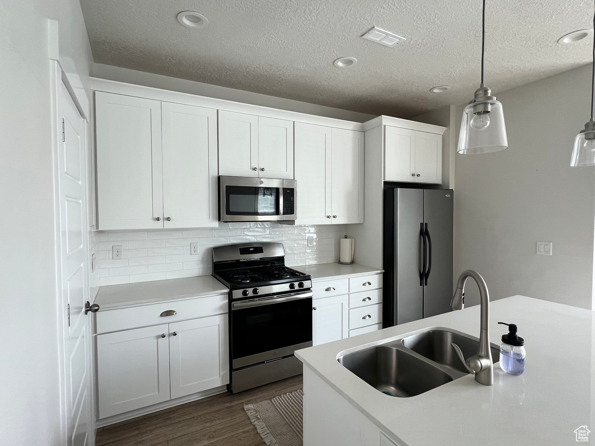 Kitchen with decorative light fixtures, hardwood / wood-style flooring, white cabinetry, appliances with stainless steel finishes, and sink