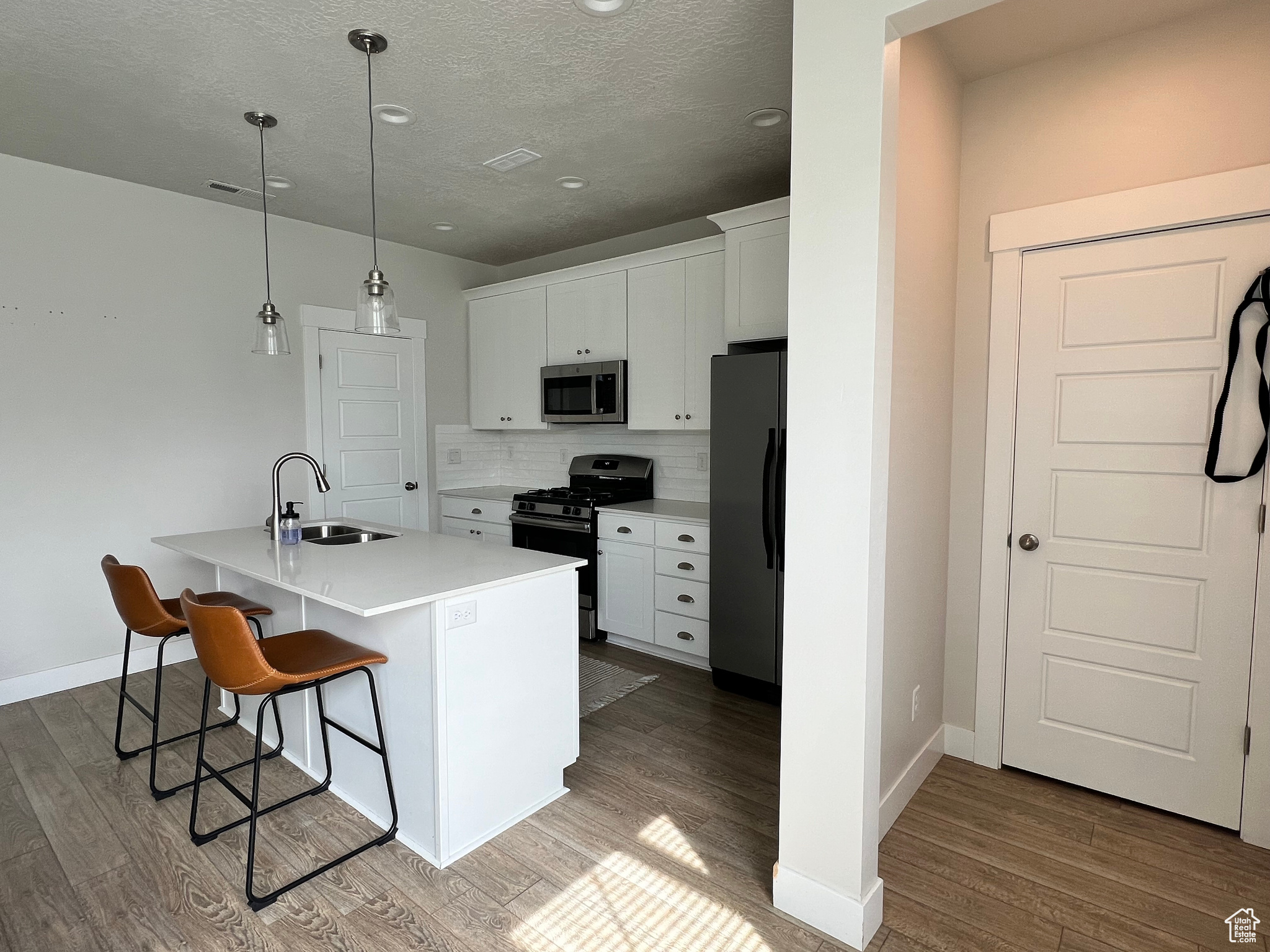 Kitchen with appliances with stainless steel finishes, white cabinets, hardwood / wood-style flooring, backsplash, and sink