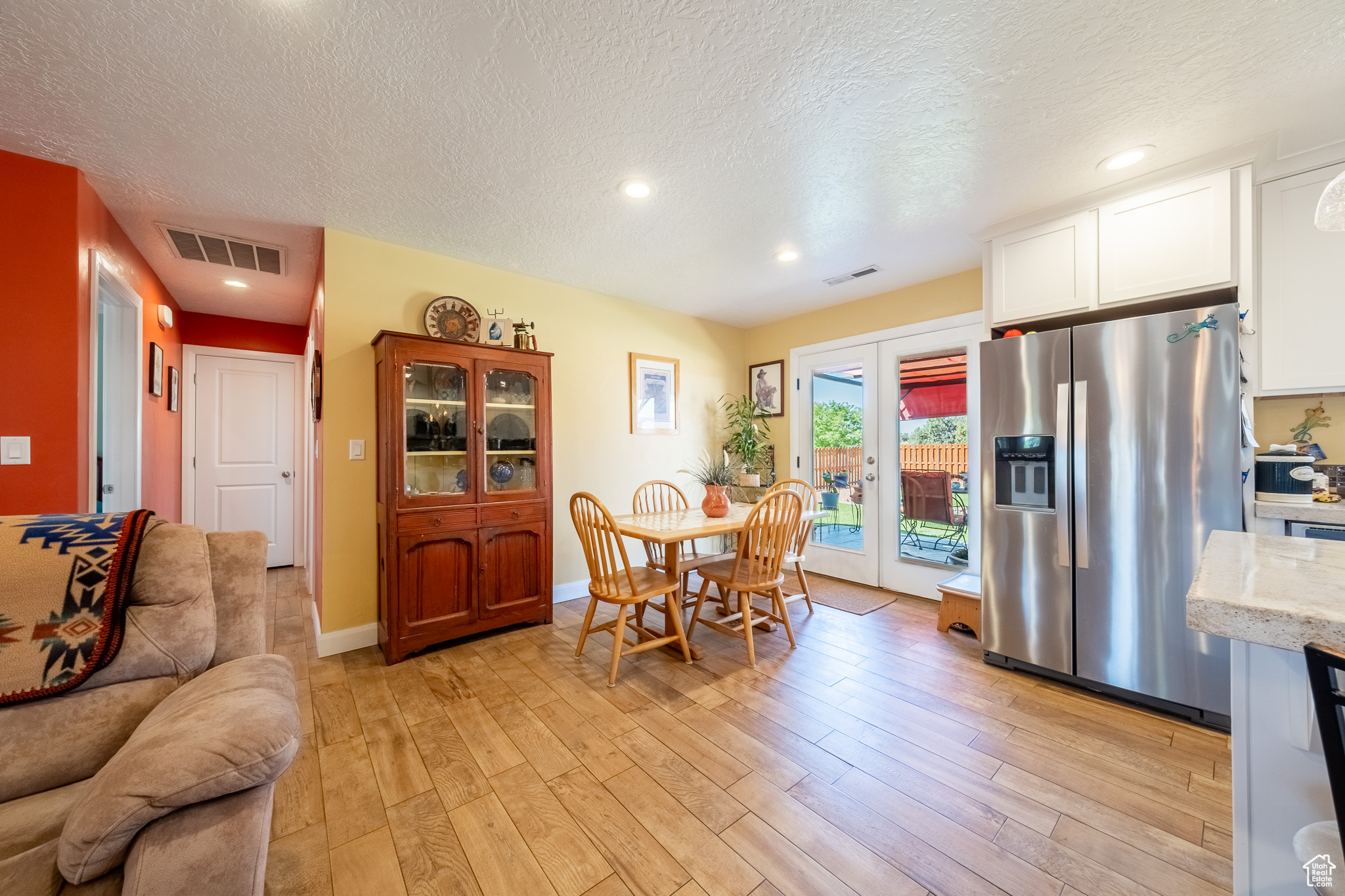 Kitchen with white cabinetry, a textured ceiling, stainless steel refrigerator with ice dispenser, and light hardwood / wood-style flooring