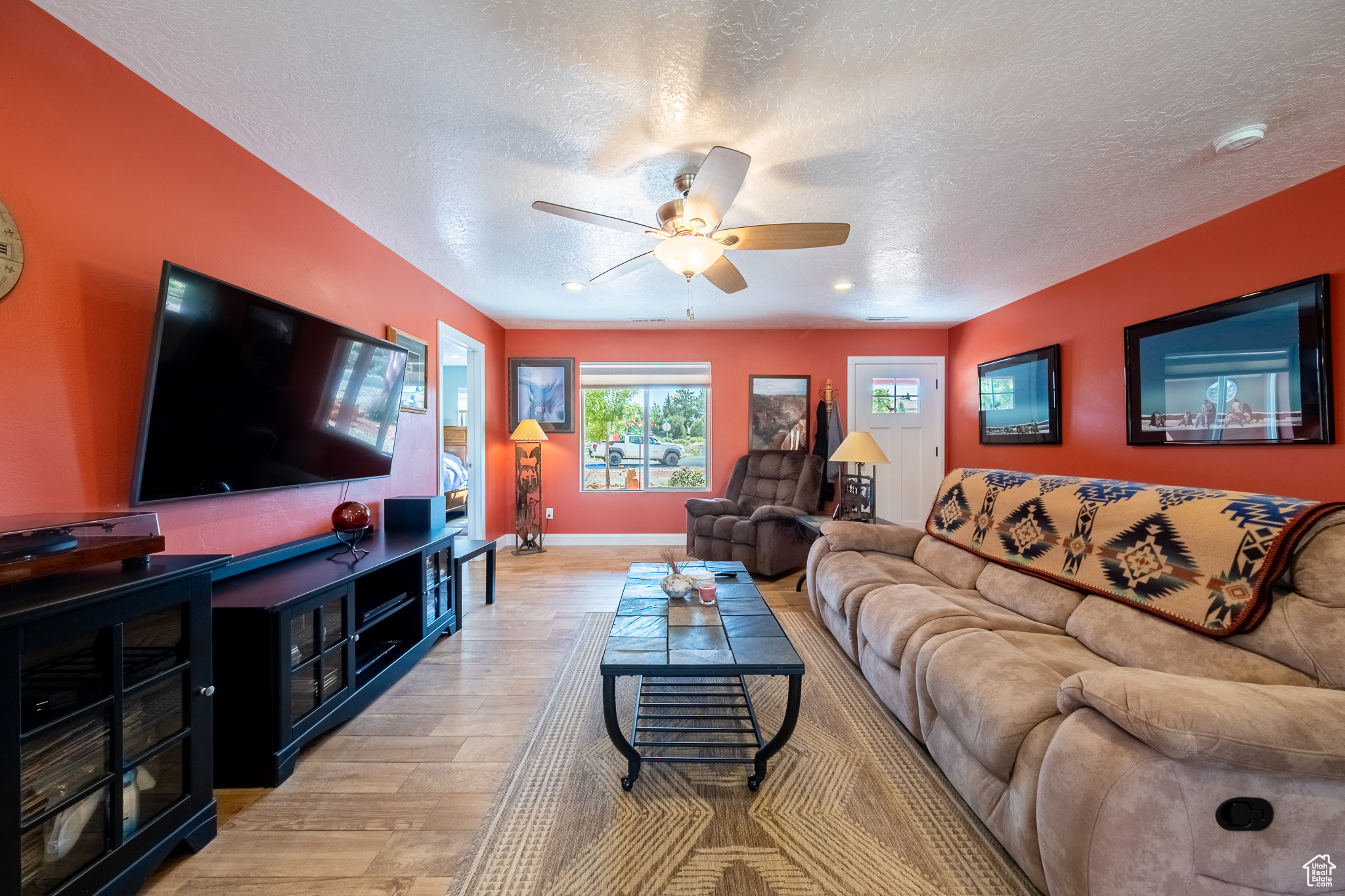 Living room with ceiling fan, a textured ceiling, and light wood-type flooring