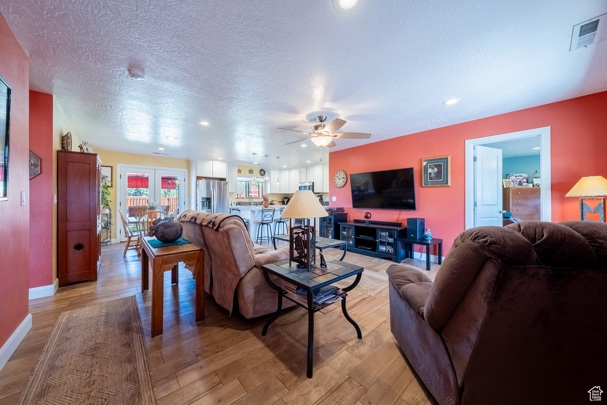 Living room with french doors, a textured ceiling, ceiling fan, and light wood-type flooring