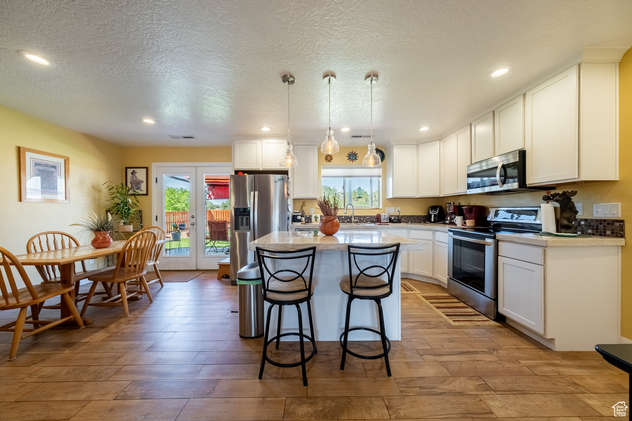 Kitchen with stainless steel appliances, decorative light fixtures, white cabinetry, and a kitchen island