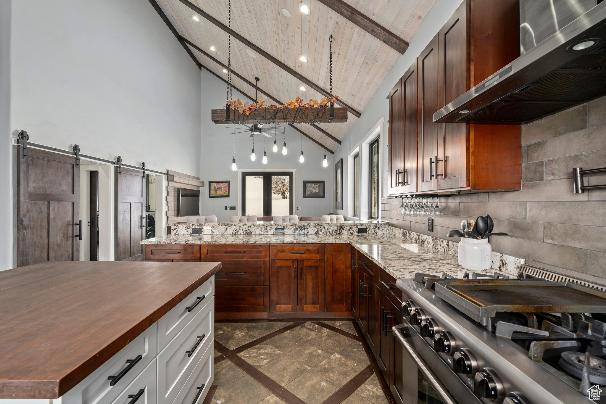 Kitchen featuring stainless steel stove, white cabinetry, wall chimney exhaust hood, beam ceiling, and a barn door