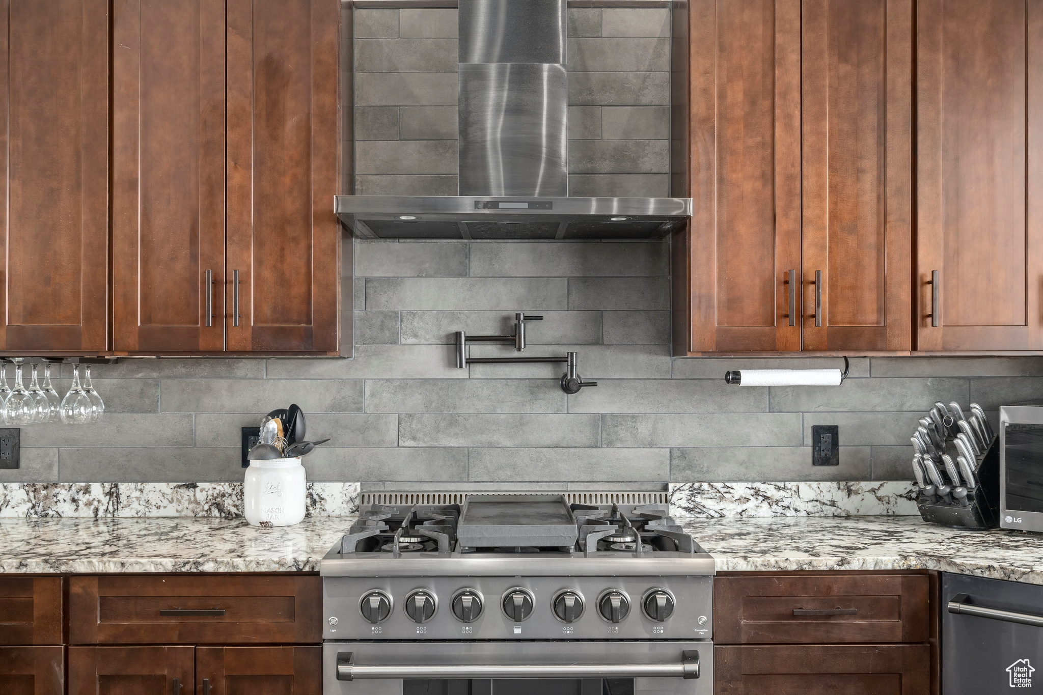 Kitchen with stainless steel range, backsplash, light stone counters, and wall chimney exhaust hood