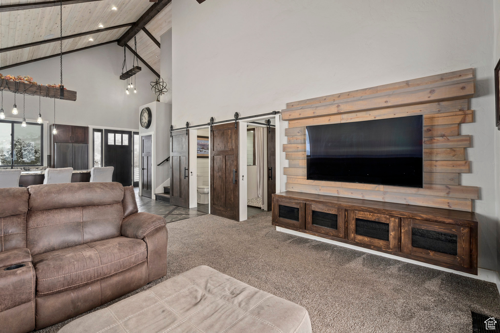 Living room with a barn door, high vaulted ceiling, carpet floors, and wooden ceiling