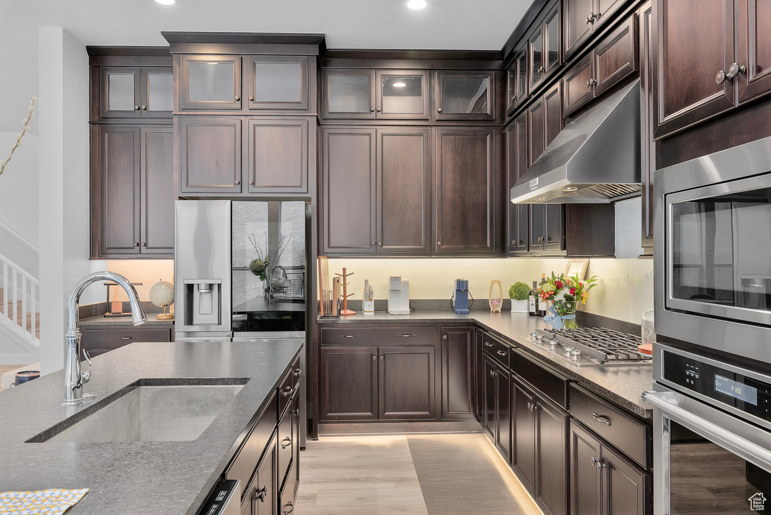 Kitchen featuring dark brown cabinets, light hardwood / wood-style flooring, stainless steel appliances, light stone counters, and sink