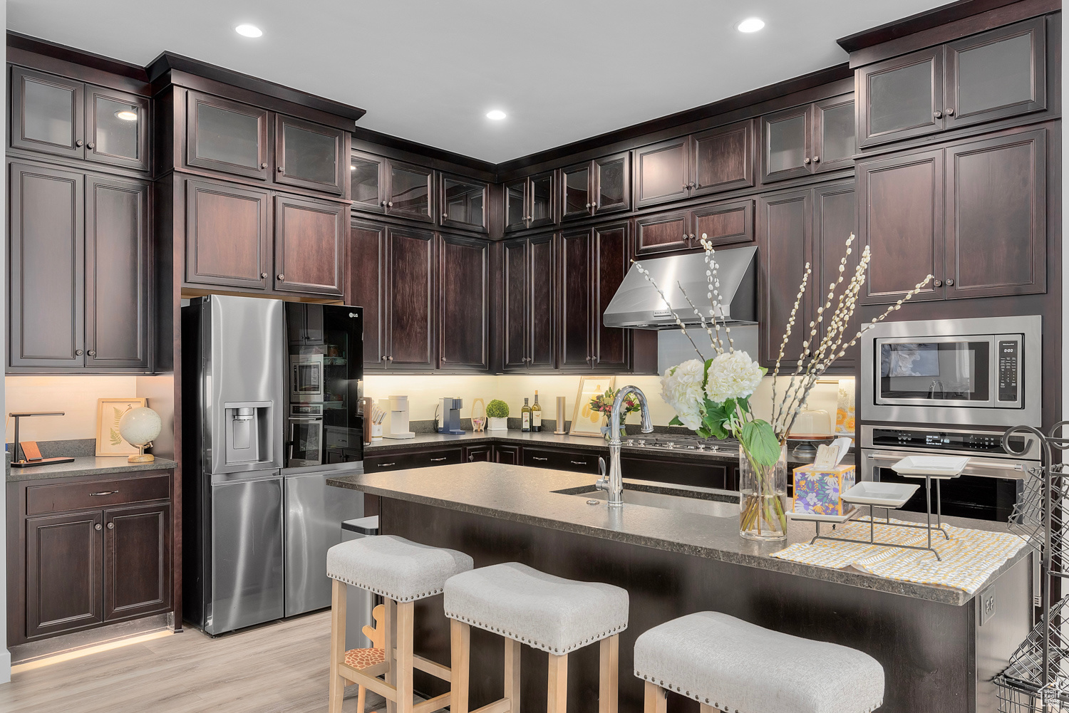 Kitchen featuring appliances with stainless steel finishes, light hardwood / wood-style floors, light stone countertops, and dark brown cabinets