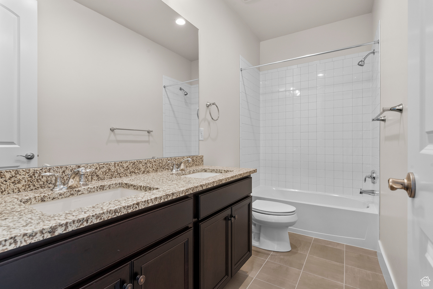 Full bathroom featuring tiled shower / bath combo, double sink vanity, toilet, and tile floors