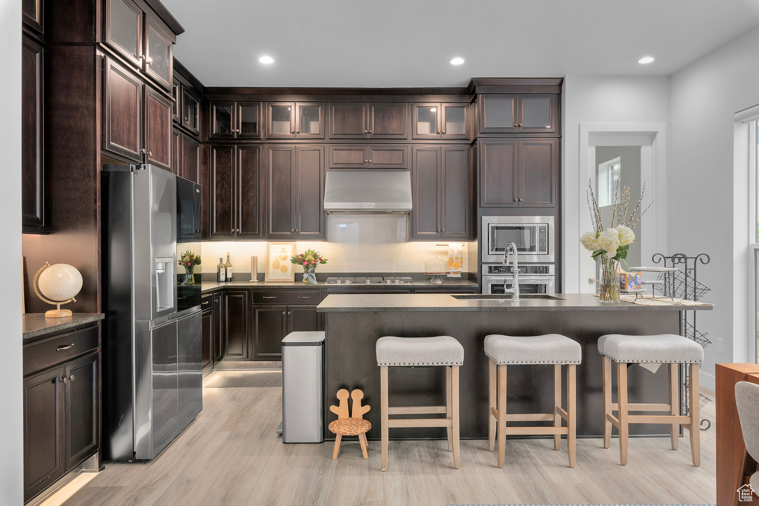 Kitchen with light hardwood / wood-style floors, a center island with sink, appliances with stainless steel finishes, dark brown cabinets, and sink