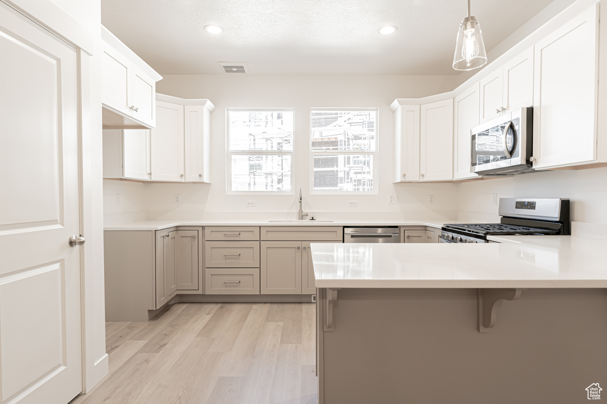 Kitchen featuring appliances with stainless steel finishes, white cabinetry, kitchen peninsula, light hardwood / wood-style flooring, and sink