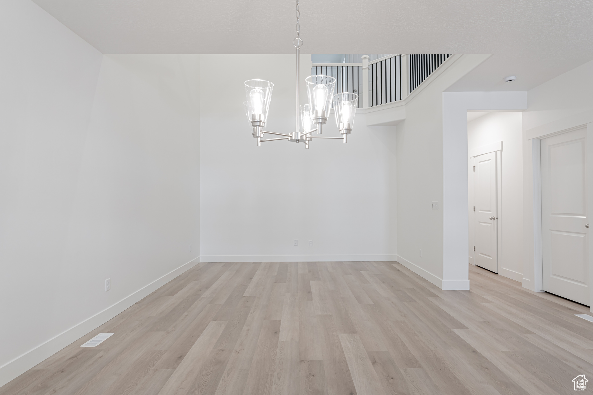 Empty room with light wood-type flooring and an inviting chandelier