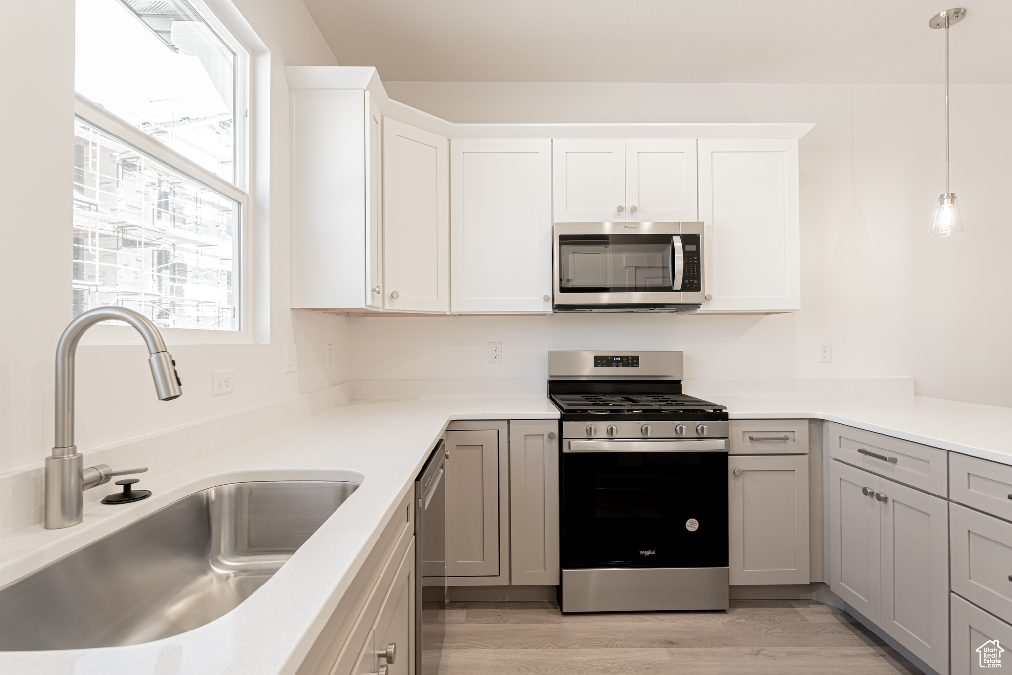 Kitchen featuring hanging light fixtures, sink, gray cabinets, stainless steel appliances, and light wood-type flooring