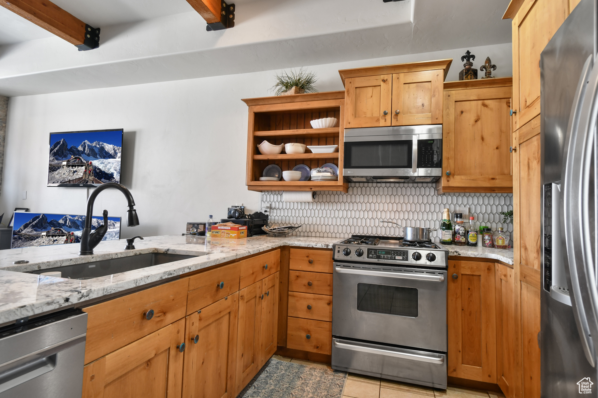 Kitchen featuring beamed ceiling, light tile flooring, backsplash, sink, and appliances with stainless steel finishes