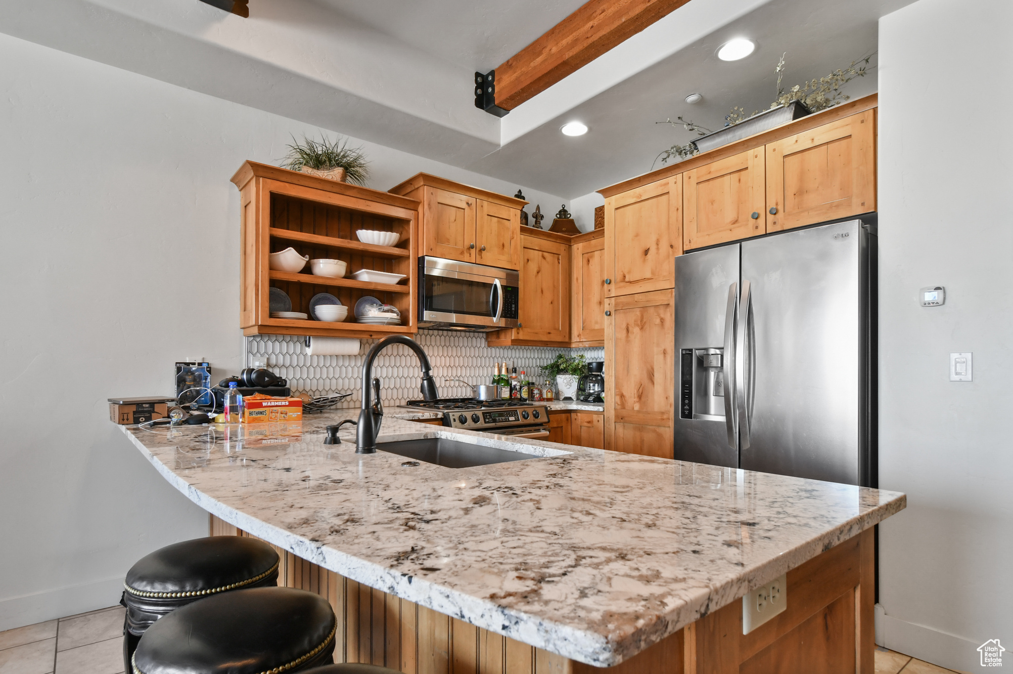 Kitchen with tasteful backsplash, kitchen peninsula, light tile floors, and stainless steel appliances