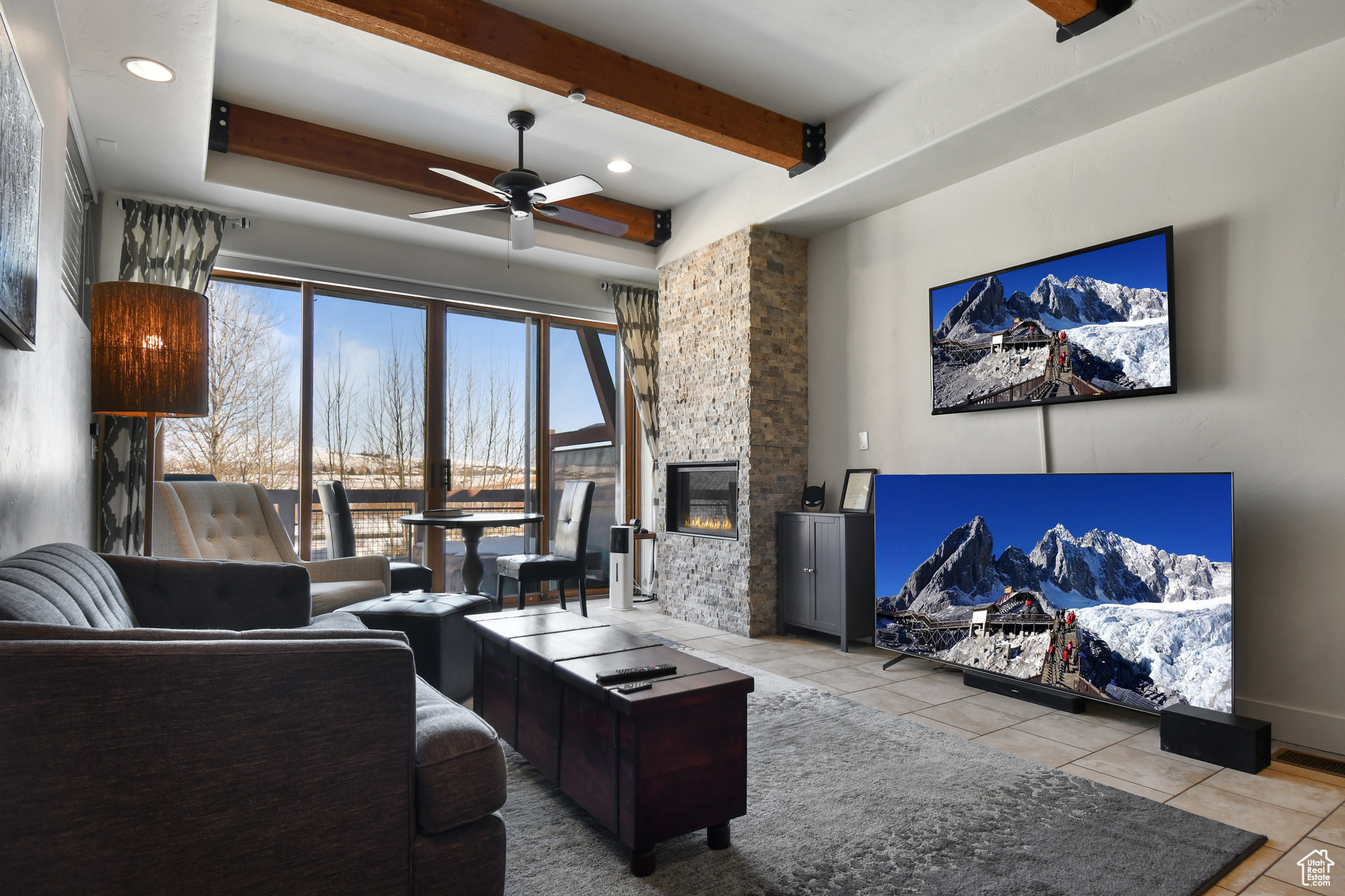 Living room featuring beam ceiling, tile floors, ceiling fan, and a fireplace